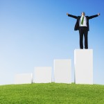 Business Man Outdoors Standing on a Bar Graph with Arms Raised