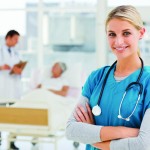 Young smiling doctor standing in hospital with colleagues talking to patient in background